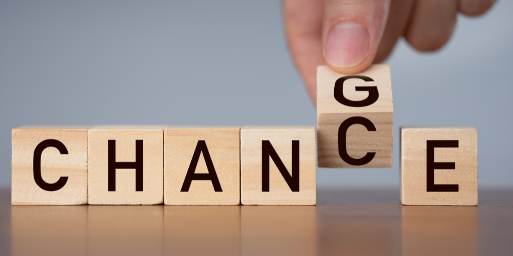 A group of six wooden blocks with a hand holding one block, making the word the blocks spell either "CHANCE" or "CHANGE."