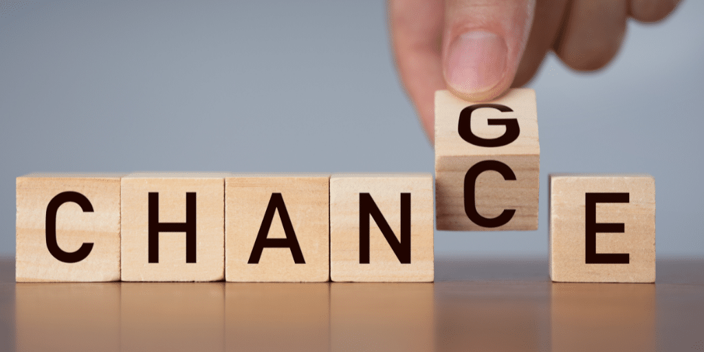A group of six wooden blocks with a hand holding one block, making the word the blocks spell either "CHANCE" or "CHANGE."